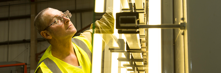 A person in a high-visibility vest and safety glasses examines illuminated tubes in an industrial setting.